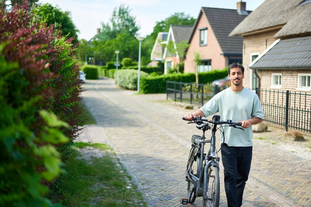 Jonge man met fiets aan de hand in een klein straatje